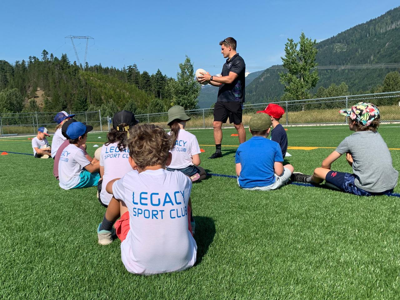 kids sitting on grass receiving instruction from soccer coach