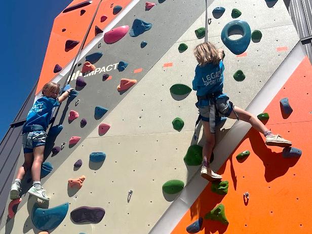 Two children in harnesses climb a colorful rock wall.