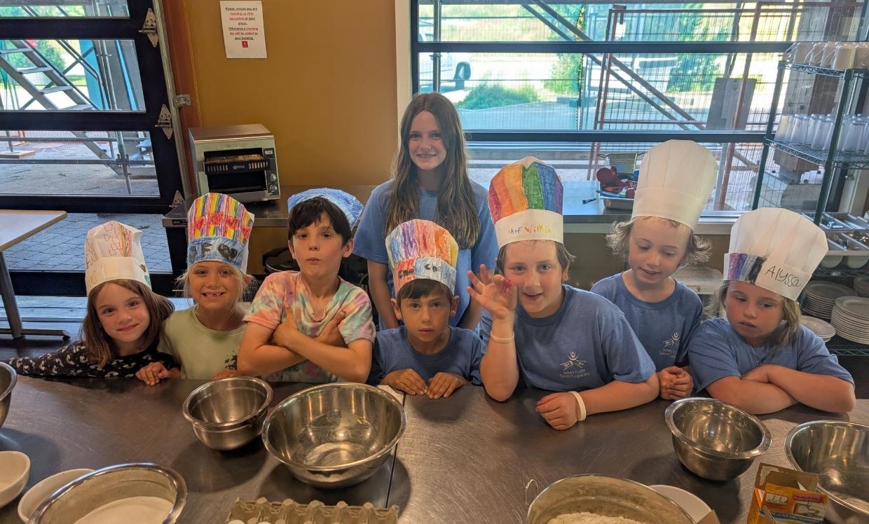 Children wearing chef hats smile behind a kitchen counter.