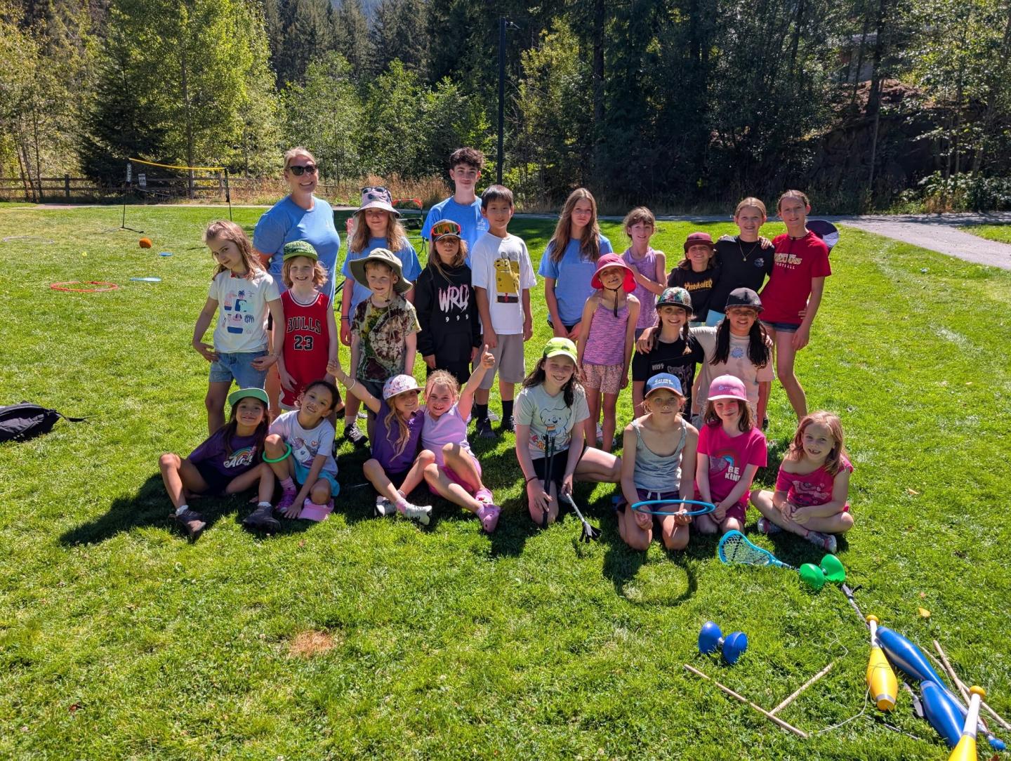 Children and adults pose on a sunny grassy field with trees in the background.