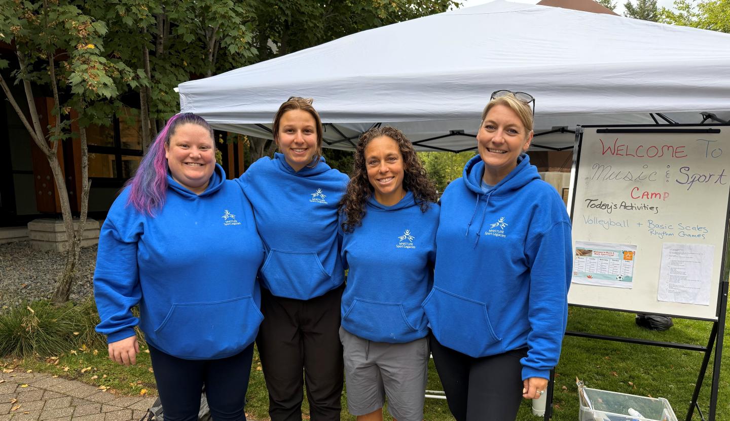 Four people in blue hoodies smiling, standing together under a white tent.