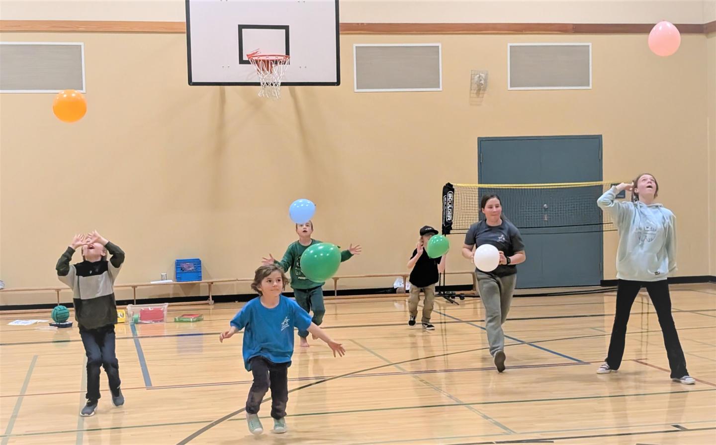 Children and adults playing with colorful balls in a school gymnasium.